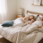 Familie liegt entspannt gemeinsam in einem hellen Bett am Morgen