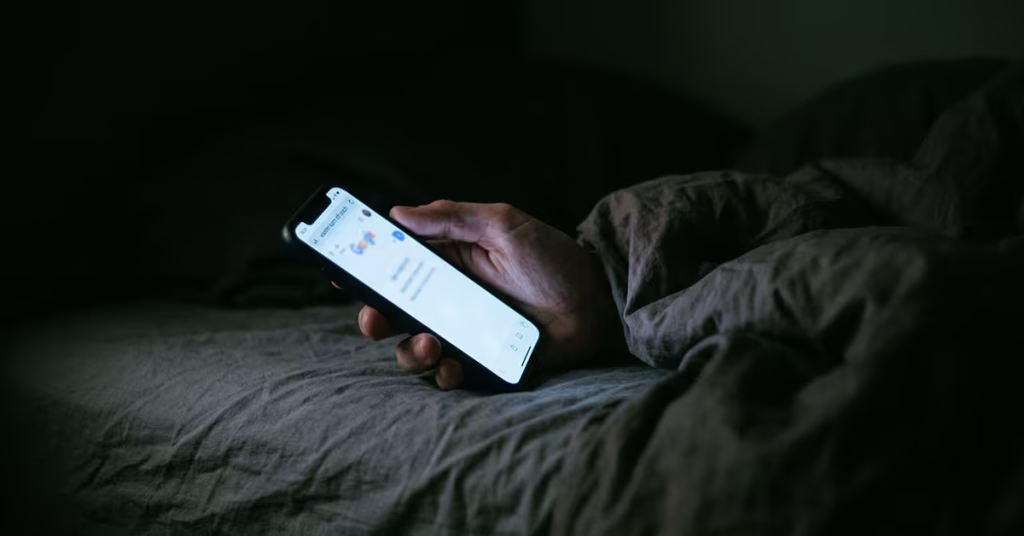 Hand mit leuchtendem Smartphone in einem dunklen Schlafzimmer mitten in der Nacht