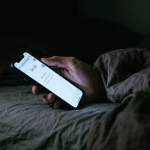 Hand mit leuchtendem Smartphone in einem dunklen Schlafzimmer mitten in der Nacht